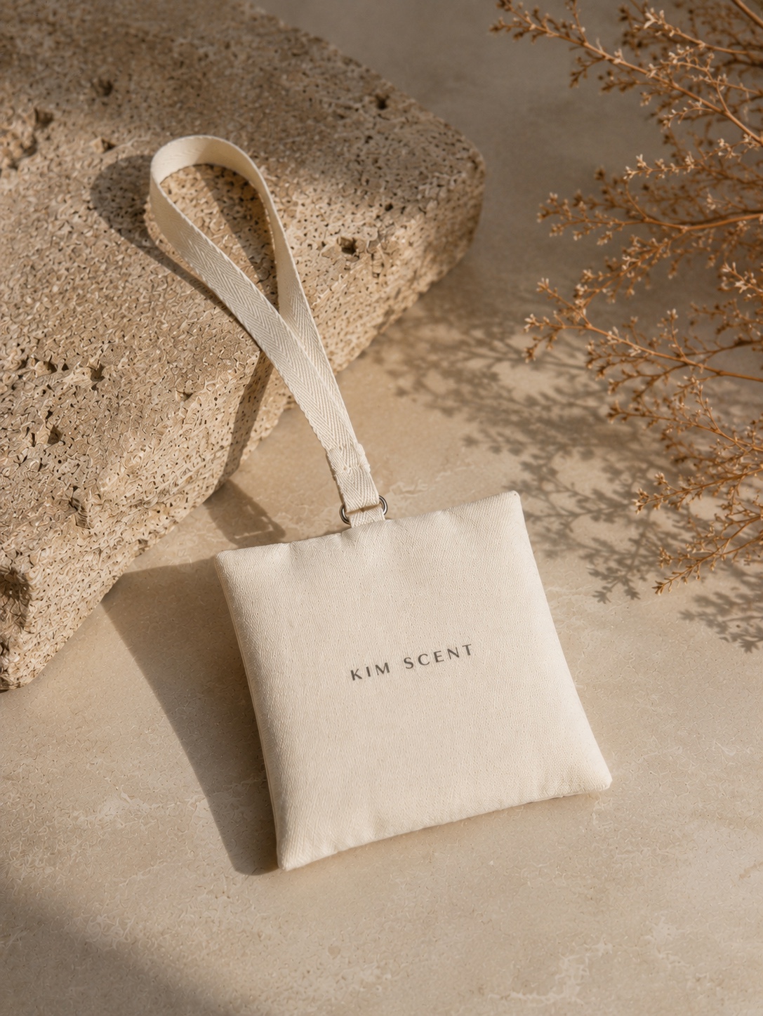 KIM SCENT sachet with a white strap on textured stone in sunlight