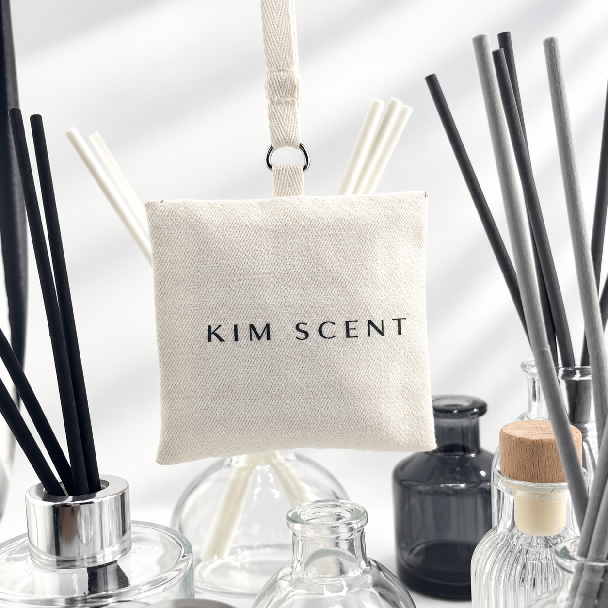 KIM SCENT fabric sachet among luminous glass bottles in the studio